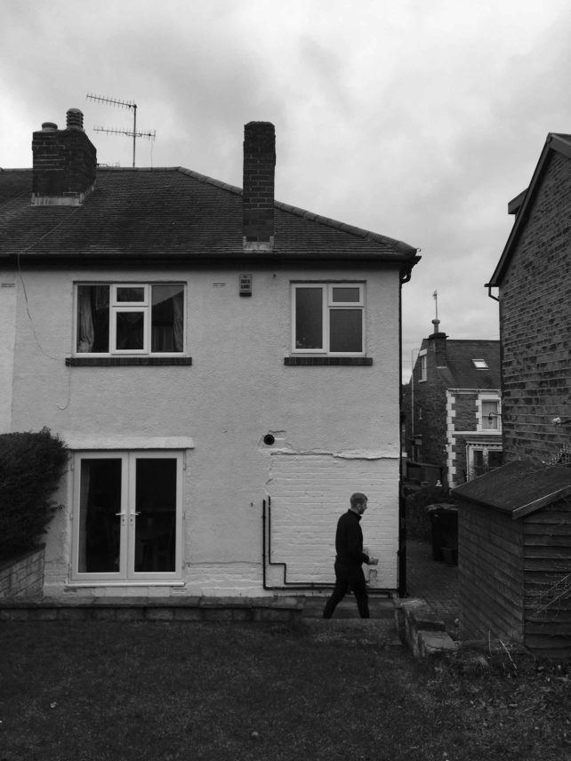Black and white image of the exterior of a semi-detached house with two windows upstairs and double doors leading to the garden.